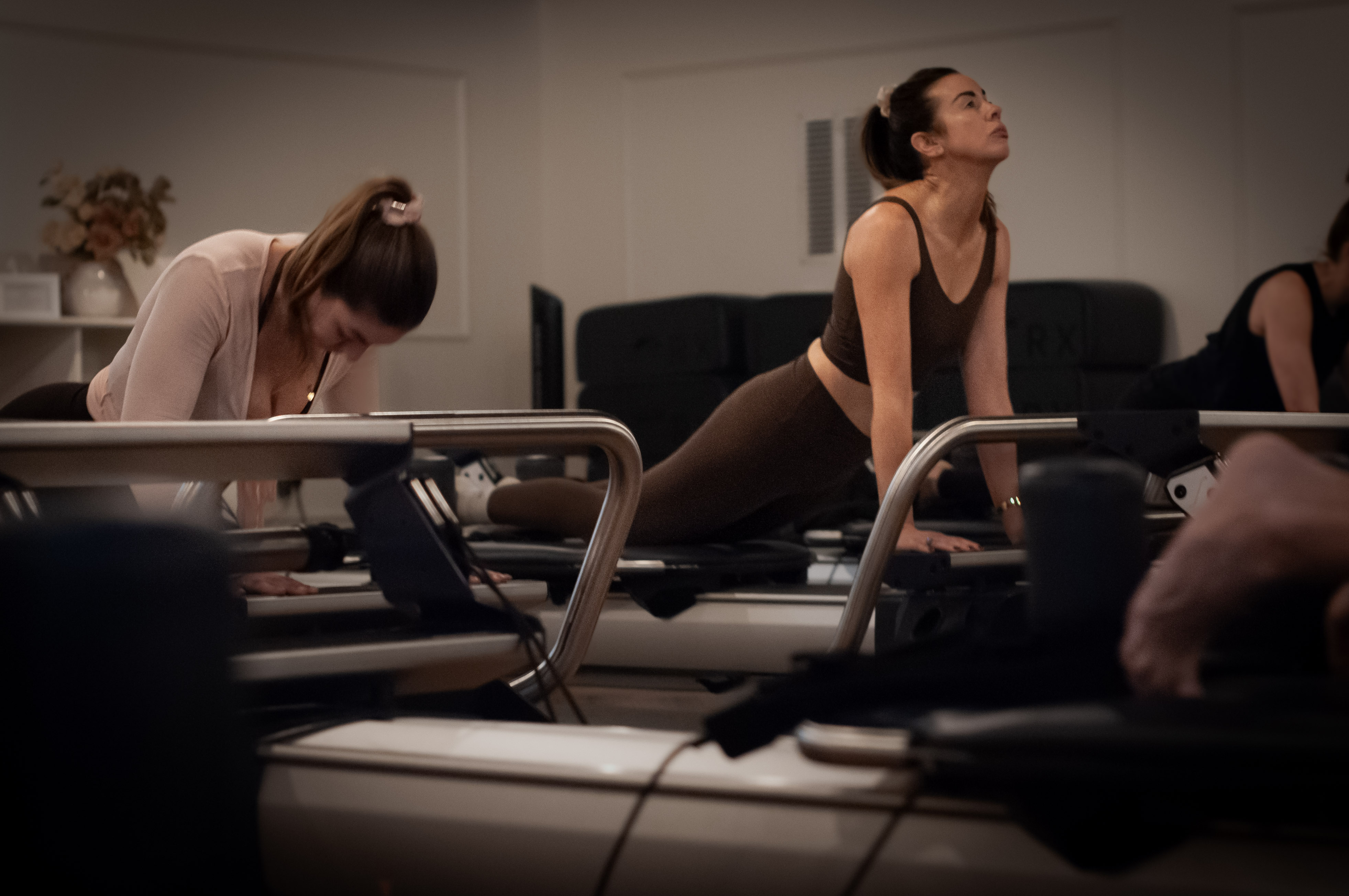 A student opening her chest upward on the Reformer, the studio busy behind her