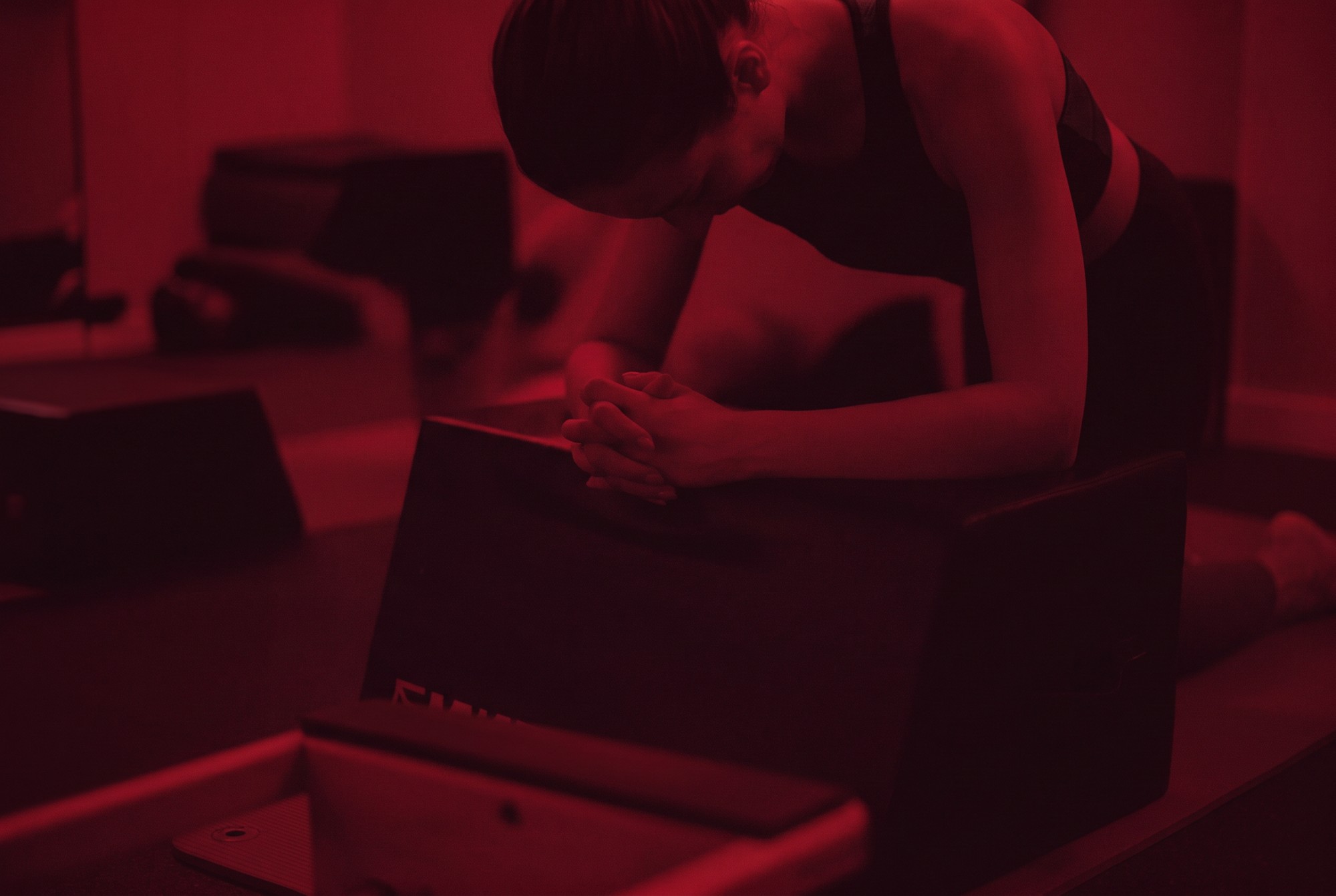 A student resting forward over a padded Pilates box, hands clasped,