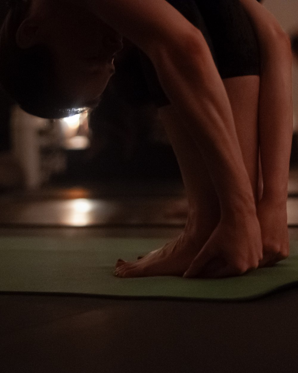 A student folding forward with palms flat beside her feet on a green mat