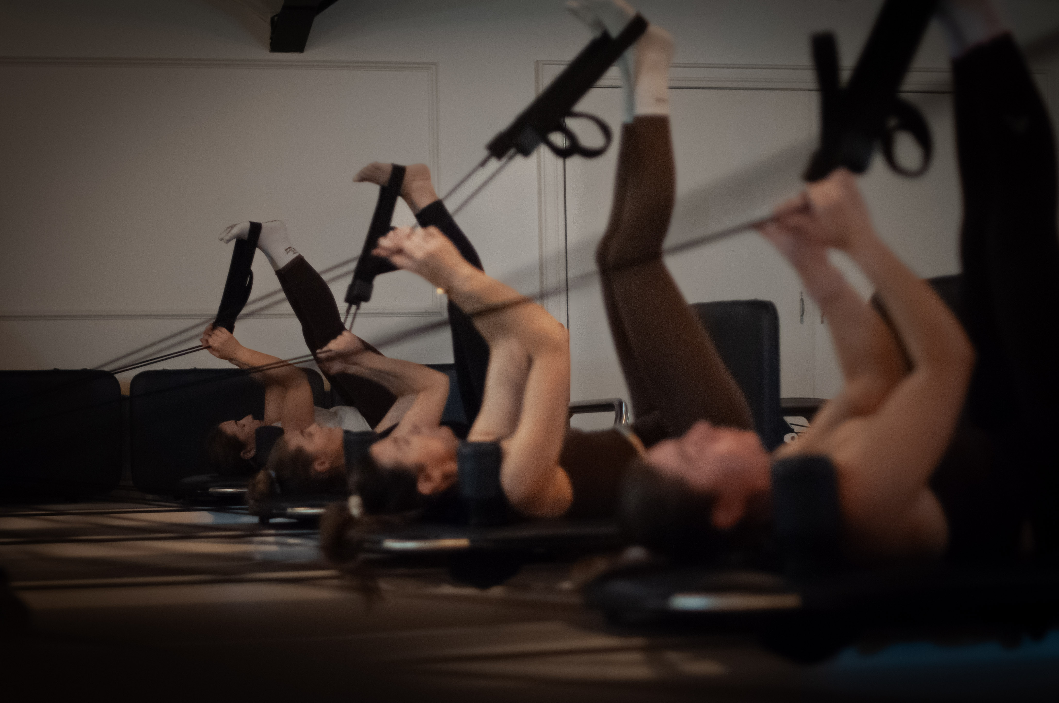 A row of students on their backs extending their legs in the Reformer straps